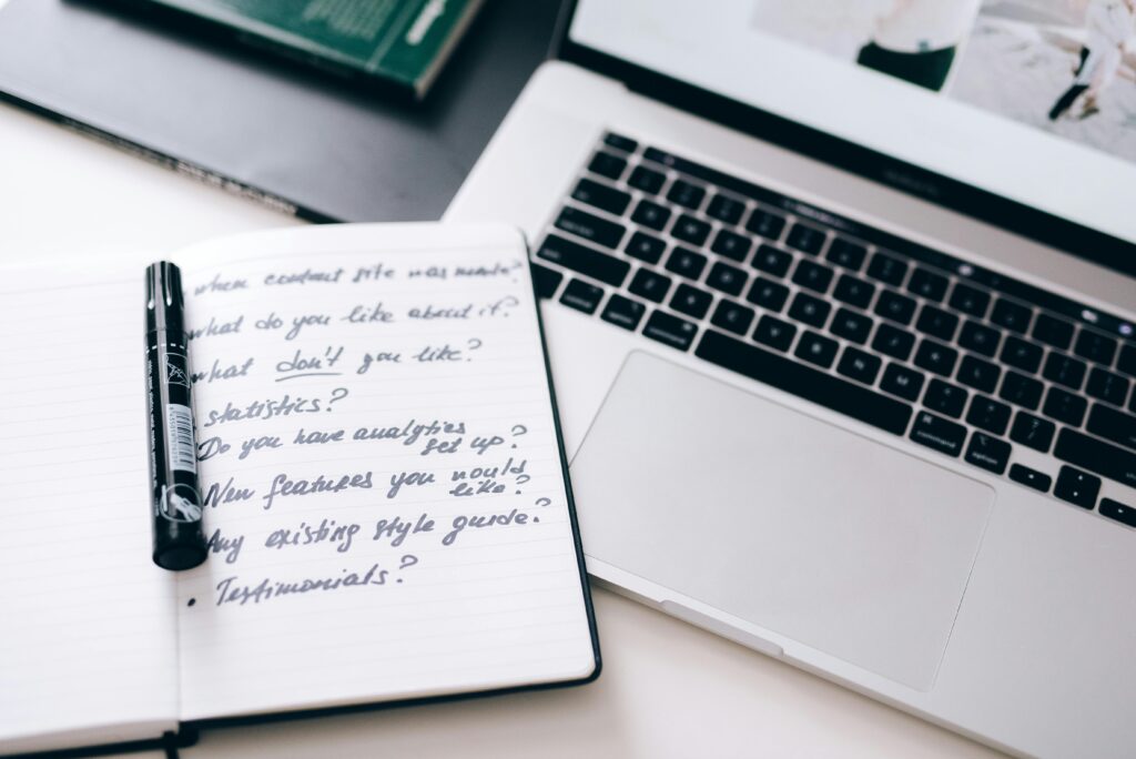 A notebook with handwritten notes next to a laptop on a workspace desk.